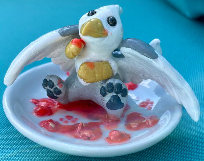 A tiny white-hand-grey gryphon sits on a plate, surrounded by the raspberry-colored remnants of a snack.