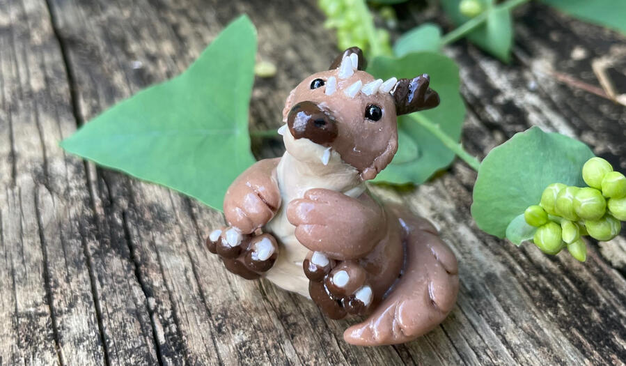 A small brown kobold sits upon a weather wooden walkway amidst greenery