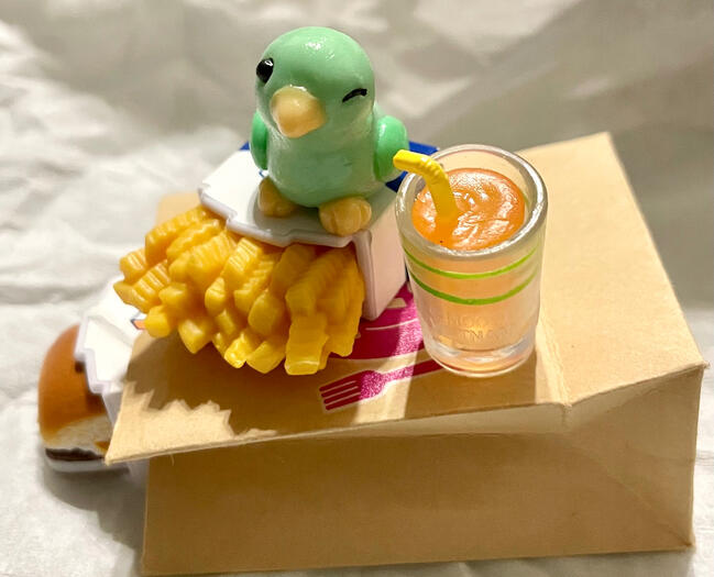 A small green parrotlet winks from atop a pile of victory snakcs