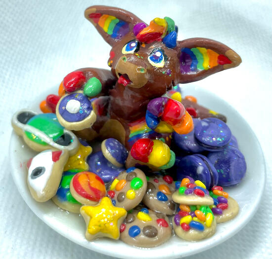 A sparkly, fluffy dragon with rainbow markings sits on a plate stacked high with space-themed cookies and desserts