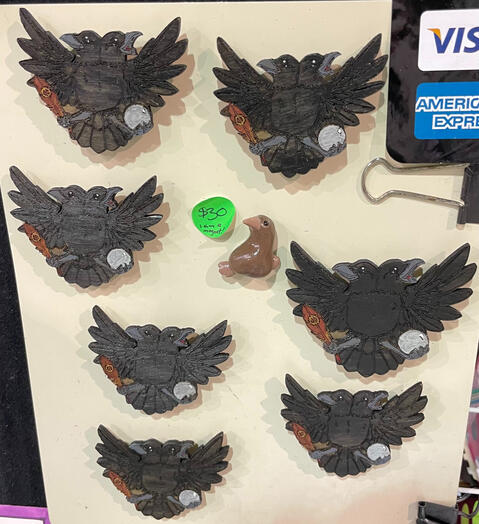 Tried out hand-painted laser-cut wooden images of the Twin Raven Crest design. (Some pin versions can be seen at bottom of MFF 2025 Sculpt Detail image.) These here were done as magnets and mounted on an improvised display (not shown on FM24 overall table