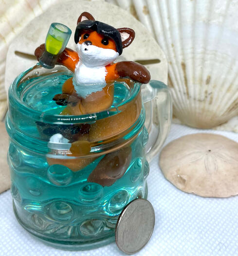 A red fox lounges inside a bubbled stein of azure liquid, a glass of lemonade in hand & sunglasses balanced atop his head