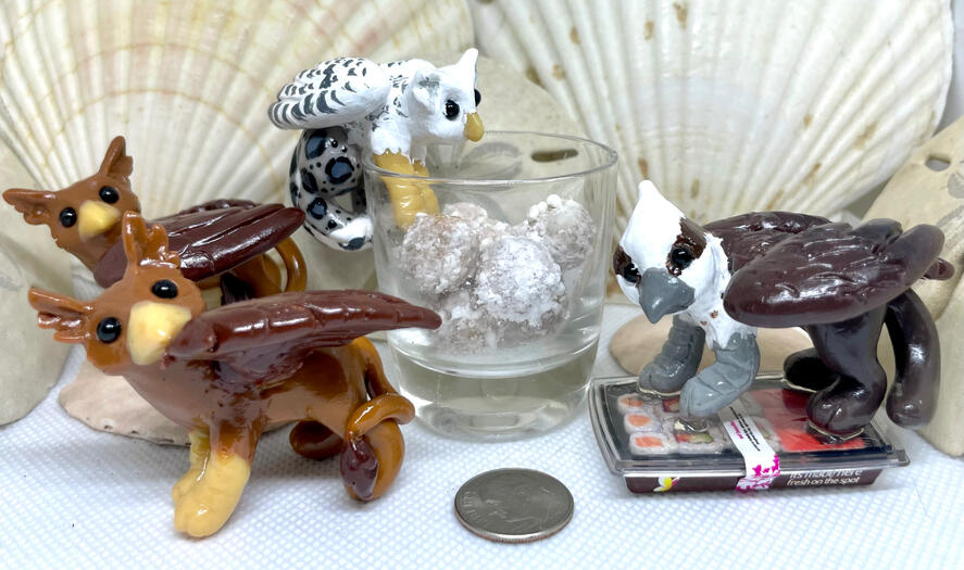 Various gryphons stand around. Two traditional brown/tawny eagle-lion morphs pause to gaze at viewer (one gently preening a wing feather), while a snow-owl/snow leopard gryphon dangles by the waist from th edge of a glass jar, reaching for snowball cookies