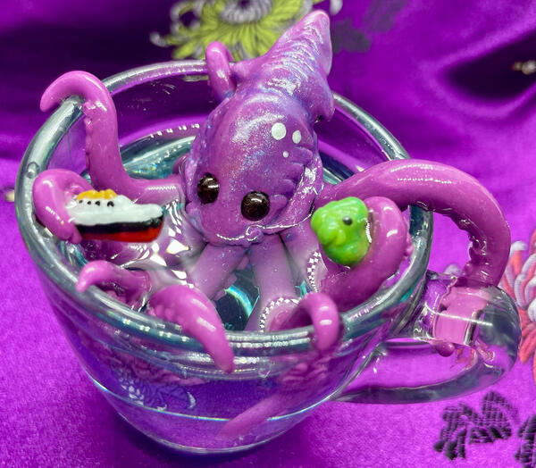 A tiny kraken in a clear glass teacup, playing w/a Titanic model ship & a Cthulu rubber duckie